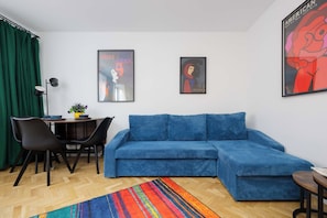 A modern living room with a blue sofa, a dining table with chairs, and two framed artworks on the wall. - Warsaw | Złota 11 | Comfortable Apartment | Downtown (Warszawa)