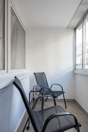 Un coin de pièce avec deux chaises en treillis noir, dont l’une est ornée d’une plante violette, et un rebord de fenêtre blanc.