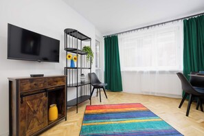 A modern living room with a flat-screen TV, a wooden cabinet, a black metal shelf with plants, a black chair, and a colorful striped rug. - Warsaw | Złota 11 | Comfortable Apartment | Downtown (Warszawa)