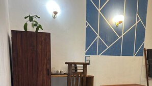 A room with a wooden desk, a chair, a bench, a trash bin, and a wall with a geometric pattern. - Rock Hill Hotel  (Unawatuna)