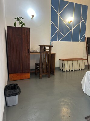 A room with a wooden desk, a chair, a bench, a trash bin, and a wall with a geometric pattern. - Rock Hill Hotel  (Unawatuna)