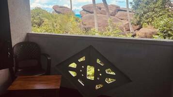 A room with a view of palm trees and rocks, a table, and a chair.