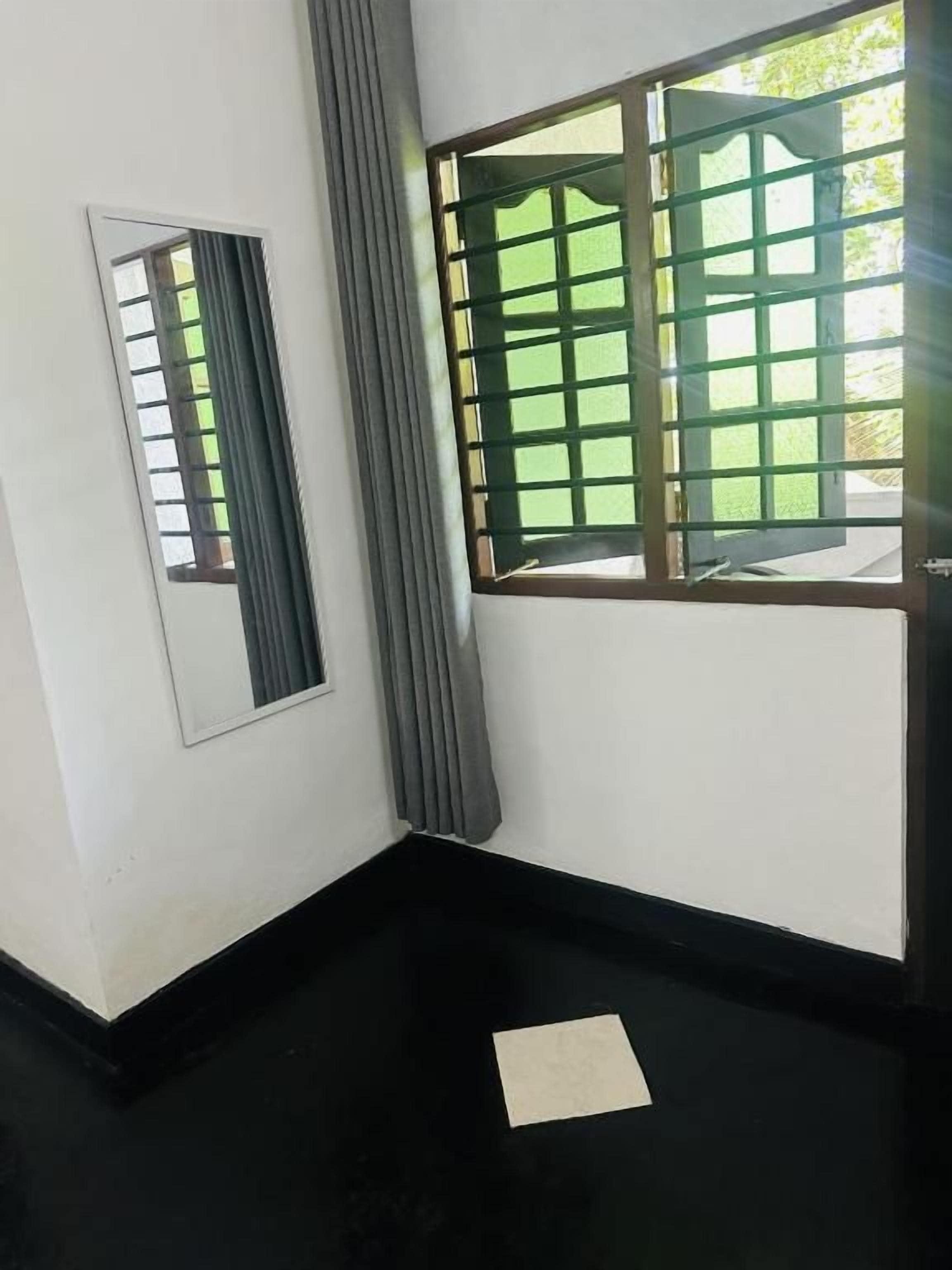 A room with a black floor, a window with metal bars, a mirror on the wall, and a piece of paper on the floor.