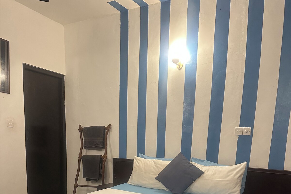 A hotel room with a bed, a chair, a desk, and a wall with vertical stripes.
