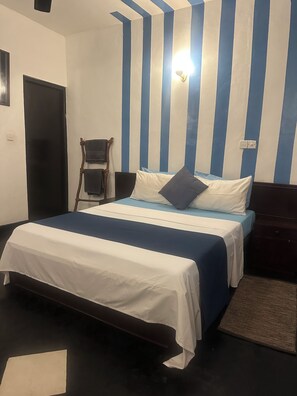A hotel room with a bed, a chair, a desk, and a wall with vertical stripes. - Rock Hill Hotel  (Unawatuna)