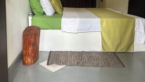 A hotel room with a bed, a green and white bedspread, a brown curtain, a wooden stool, a rug, and a wall with circular decorations. - Rock Hill Hotel  (Unawatuna)