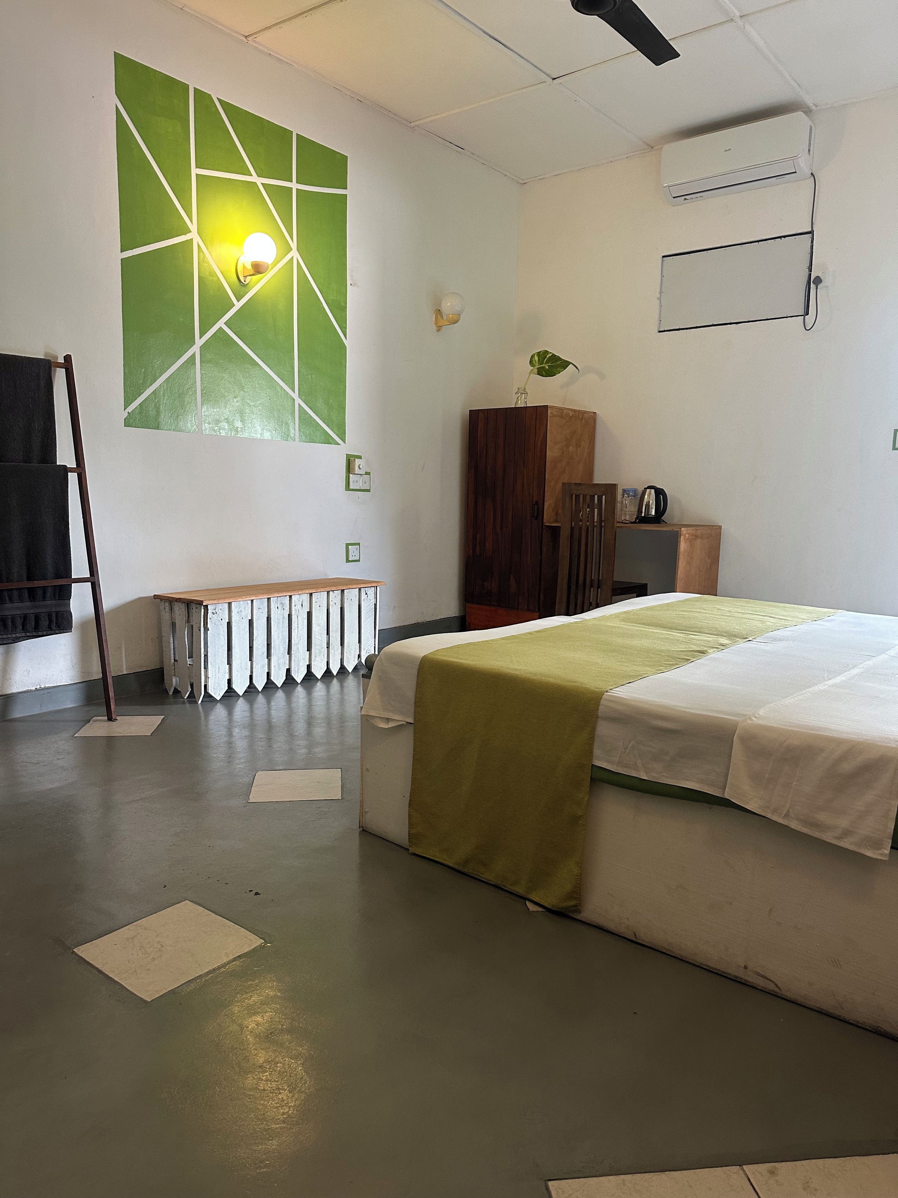 A room with a bed, a radiator, a wall-mounted air conditioner, and a green wall feature.