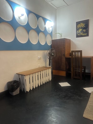 A room with a wooden bench, a fan, a cabinet, and a wall with circular mirrors. - Rock Hill Hotel - Unawatuna (Unawatuna)