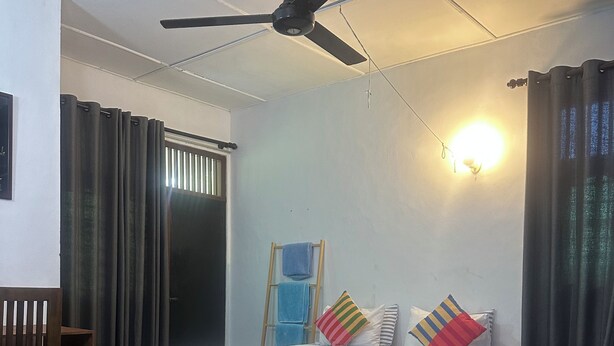 A room with two beds, a ceiling fan, a window with curtains, and a wall-mounted light. - Rock Hill Hotel  (Unawatuna)