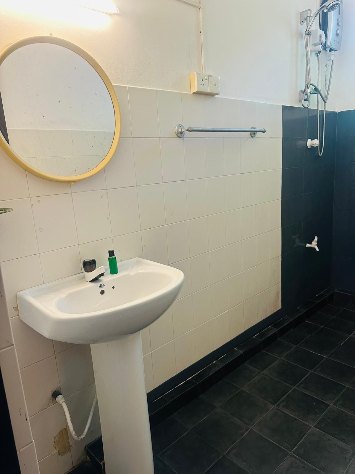 A bathroom with a white sink, a round mirror, a towel rack, and a shower area.