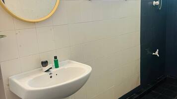 A bathroom with a white sink, a round mirror, a towel rack, and a shower area.