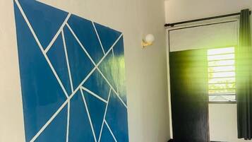 A hotel room with a large geometric wall art, a bed, a window with curtains, and a door.