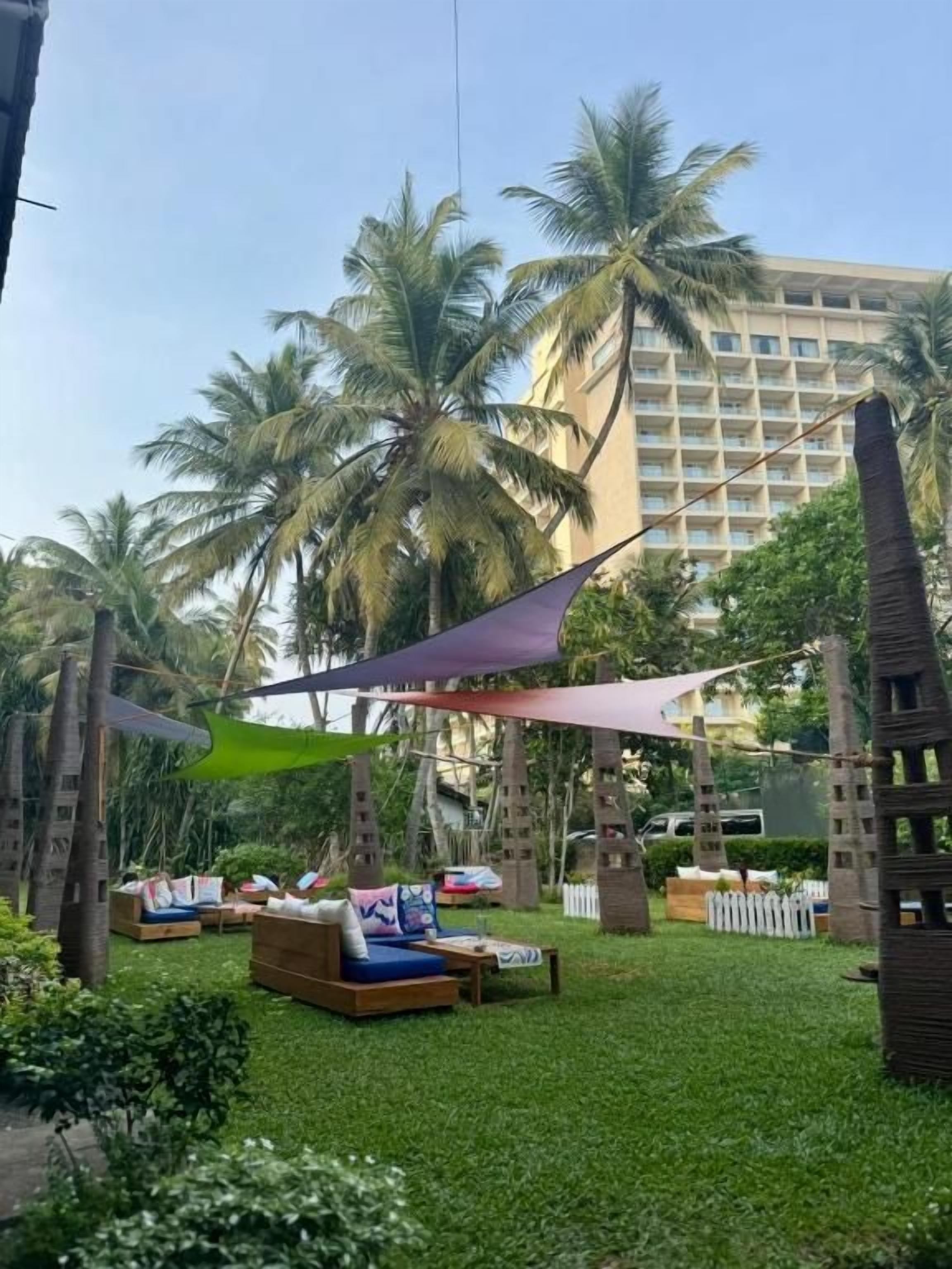 A hotel courtyard with outdoor seating, palm trees, and a building in the background.