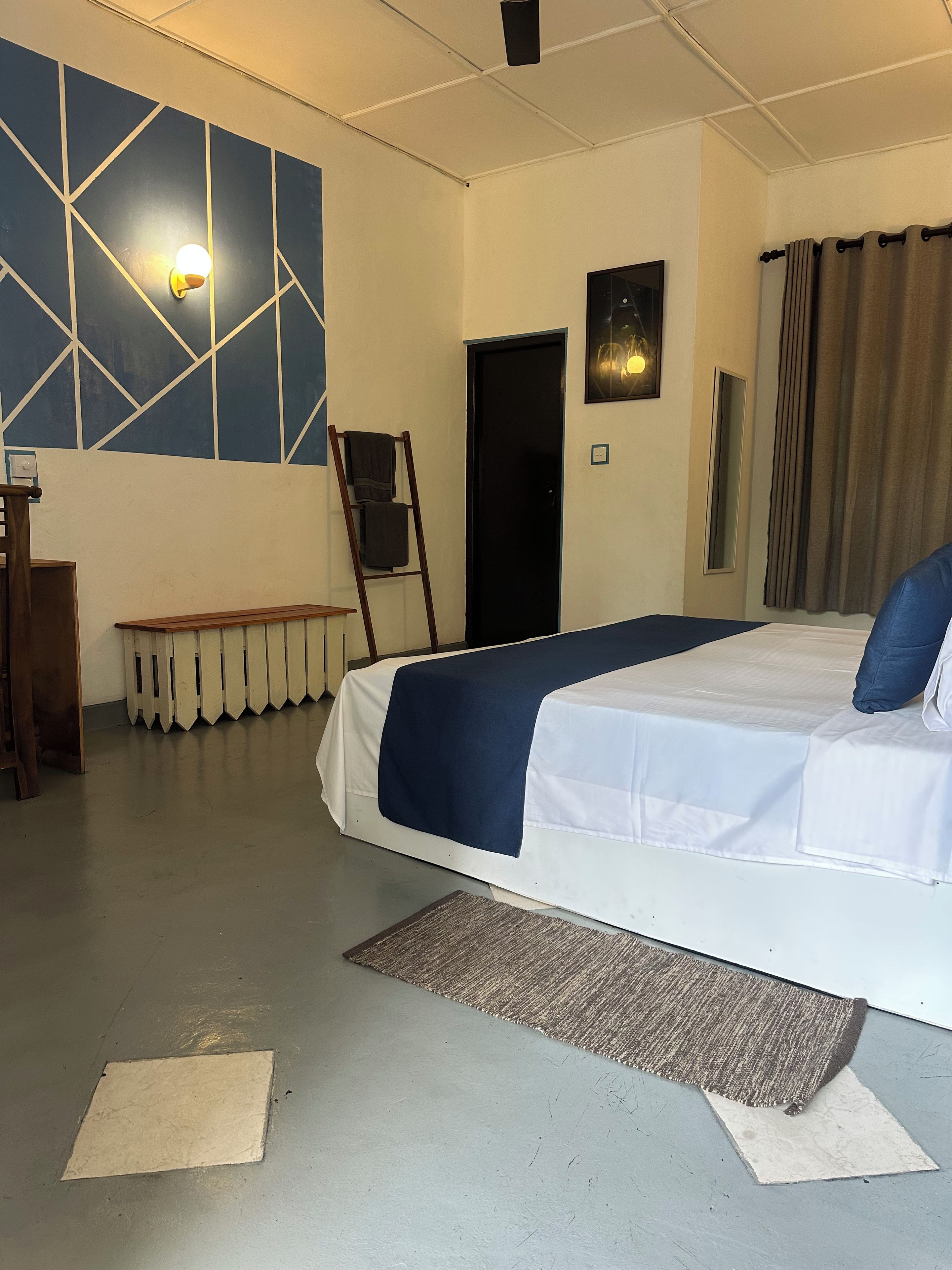 A hotel room with a bed, a bench, a ladder, a wall with geometric patterns, and a door.