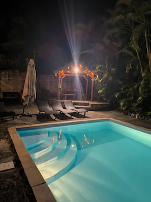 Une piscine avec des chaises longues et un espace salon abrité.