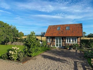 Een huis met een rood pannendak, een grindpad en een tuin met verschillende planten.