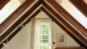Ein Schlafzimmer mit schrägem Dach, einem Bett, einer Kommode und einem Fenster mit Vorhängen.