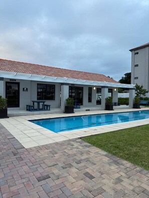 Un edificio con piscina, mobiliario exterior y un patio cubierto.