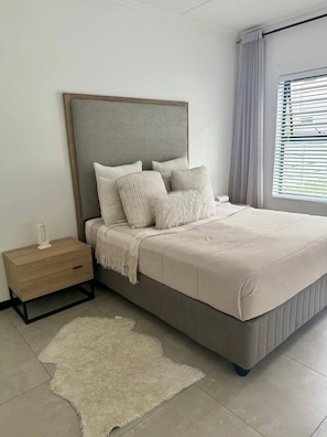 Un dormitorio con cama, mesita de noche y un amplio ventanal con cortinas.