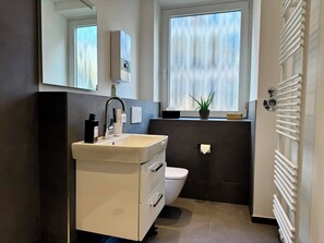 Ein modernes Badezimmer mit einem weißen Waschbecken, einer Toilette, einem Spiegel und einem Fenster mit Blick nach draußen.