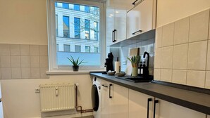 A modern kitchen with a window, a radiator, a washing machine, and a countertop with various items. - Stylish Flat • Central • 6 Guests • 65sqm (Hanover)