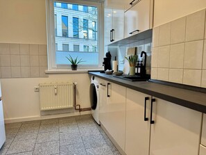 Eine moderne Küche mit Fenster, Heizkörper, Waschmaschine und einer Arbeitsplatte mit verschiedenen Gegenständen.