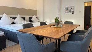 A modern hotel room with a wooden dining table, grey upholstered chairs, a bed with white bedding, and a small potted plant on the table. - Stylish Flat • Central • 6 Guests • 65sqm (Hanover)