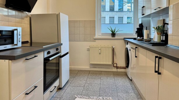 A modern kitchen with a built-in oven, microwave, and a window providing natural light. - Stylish Flat • Central • 6 Guests • 65sqm (Hanover)