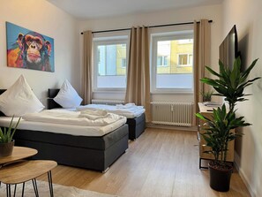 Ein modernes Schlafzimmer mit einem Bett, zwei Nachttischen, einem Sessel, einer Heizung und einem großen Fenster.