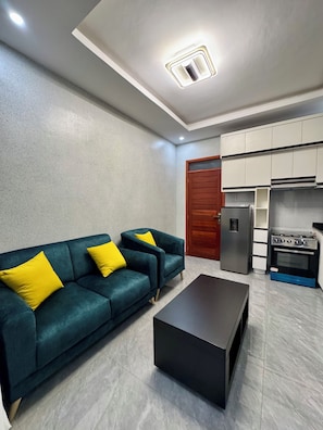 Una sala moderna con sofá, mesa de centro y área de cocina con armarios y electrodomésticos.