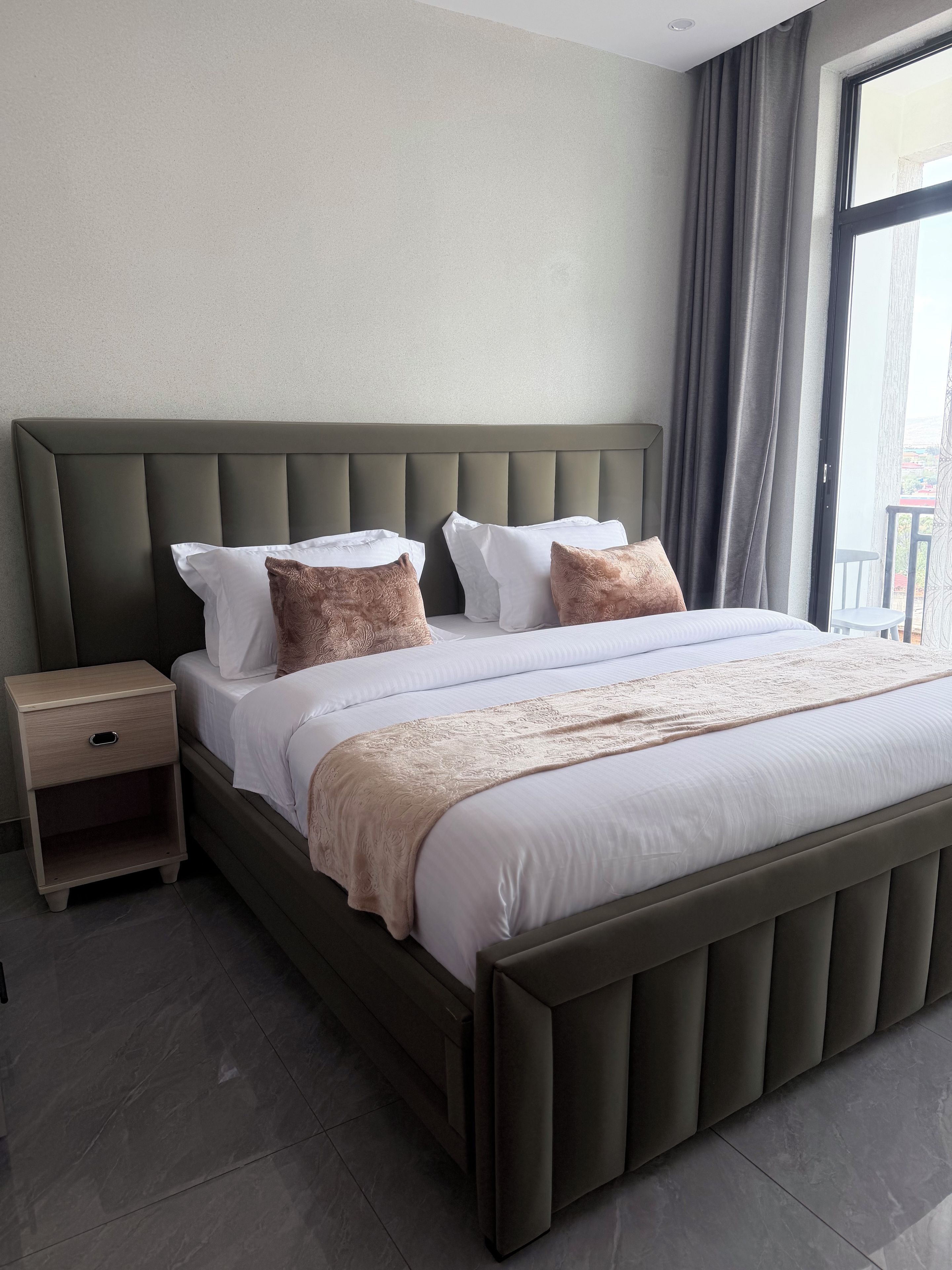 Hotellihuone, jossa on suuri sänky, yöpöytä ja näkymä ulos.