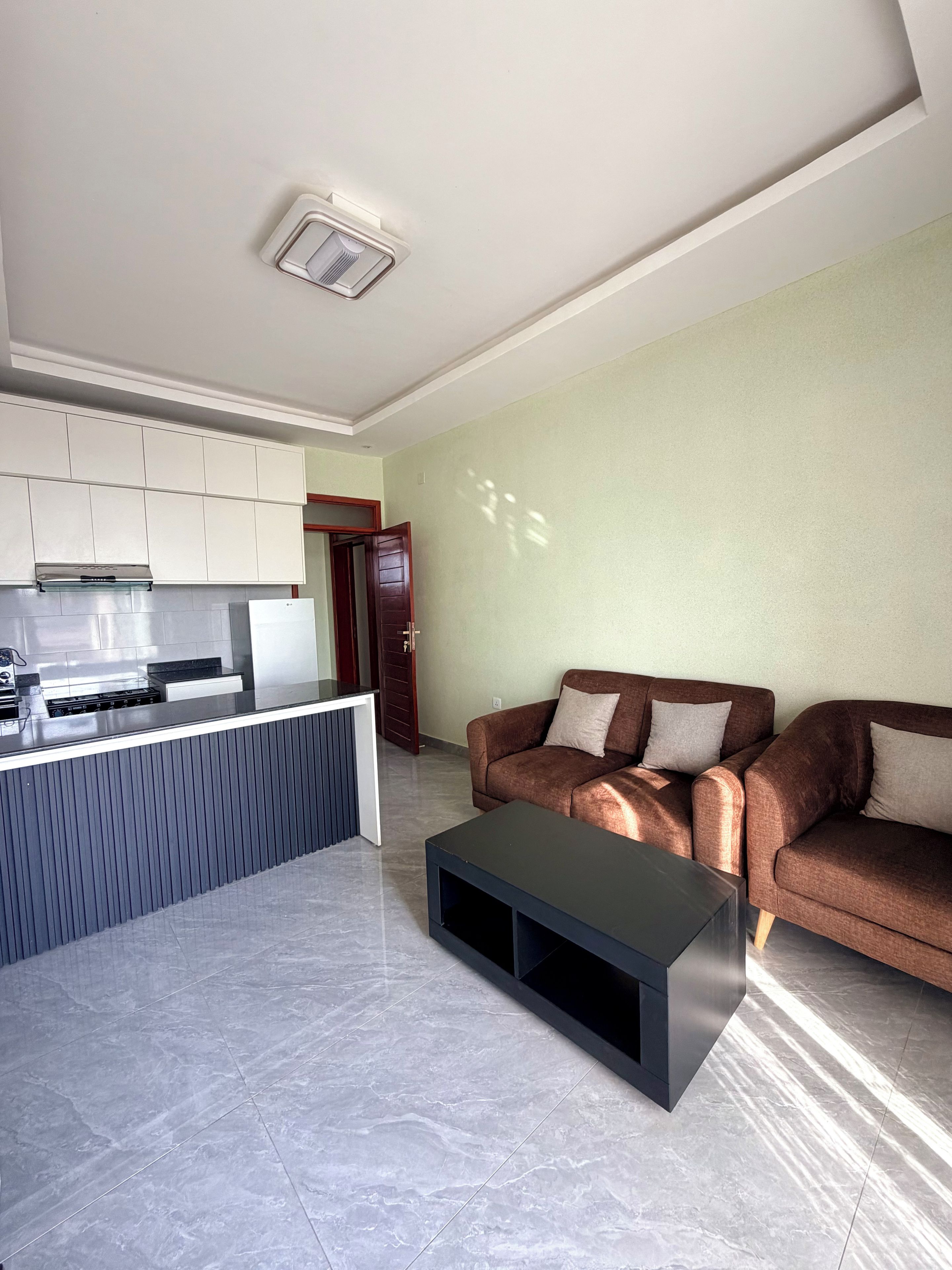A modern living room with a sofa, a coffee table, and a kitchen area with cabinets and a stove.
