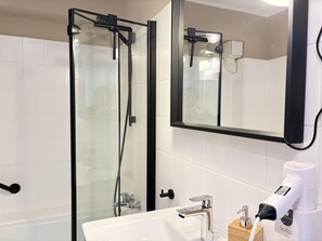 Un baño moderno con ducha envuelta en vidrio, un lavabo blanco con grifo cromado y un secador de pelo en la encimera.