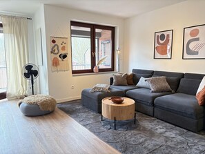 Una sala de estar moderna con un sofá gris, una mesa de centro redonda de madera y un otoman gris.