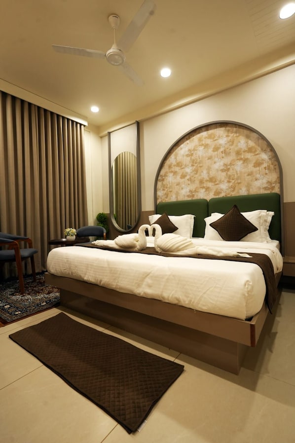 A modern hotel room with a large bed, a round headboard, a ceiling fan, and a view of the outdoors. - Hotel The Dwarka palace (Dwarka)