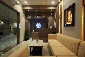 A hotel lobby with a reception desk, seating area, and a wall-mounted clock. - Hotel The Dwarka palace (Dwarka)