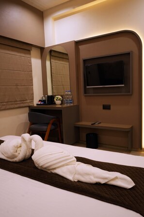 A hotel room with a bed, a desk, a chair, a TV, and a mirror. - Hotel The Dwarka palace (Dwarka)
