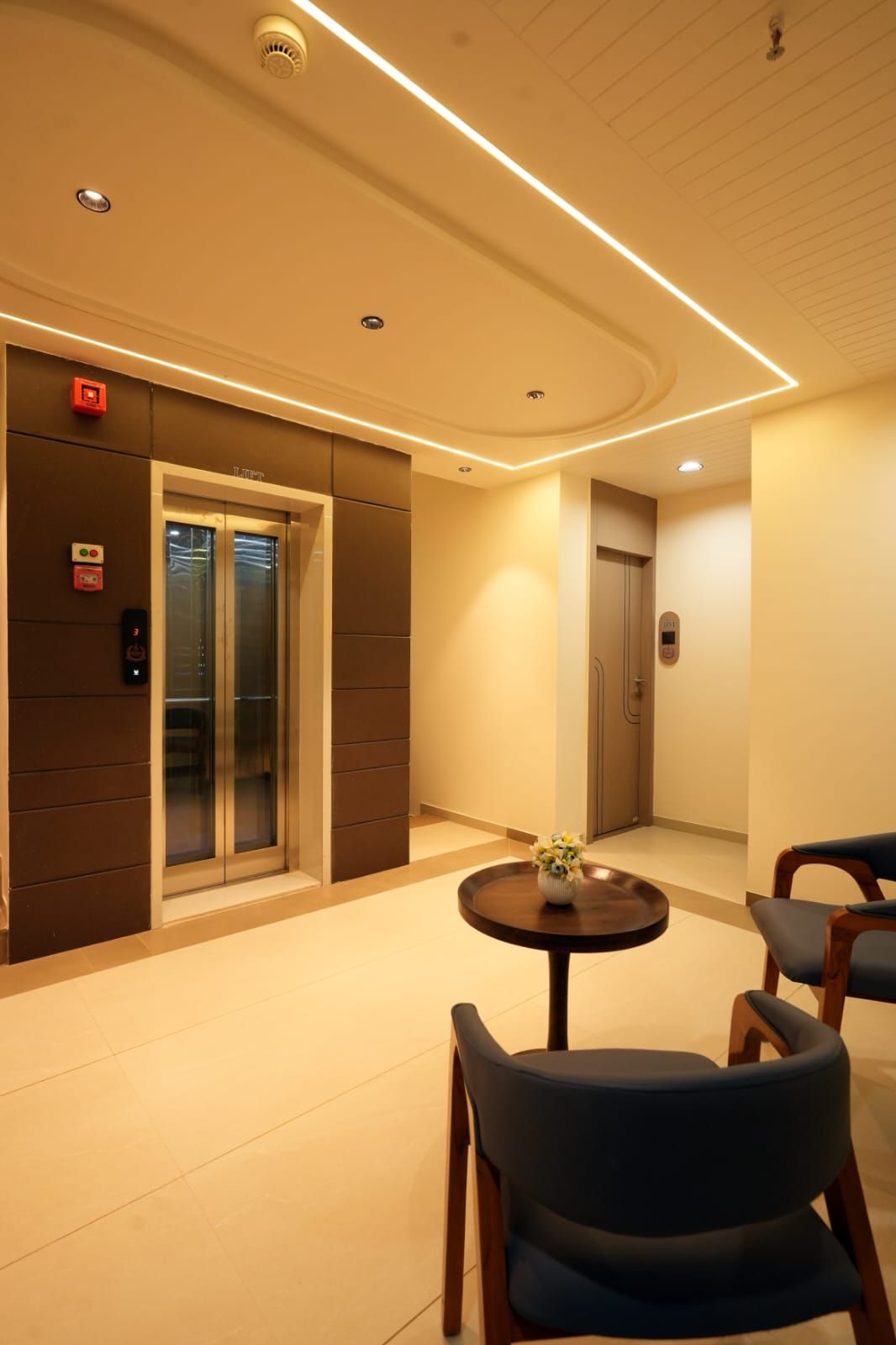 A hotel lobby with an elevator, a reception desk, and a seating area with chairs.