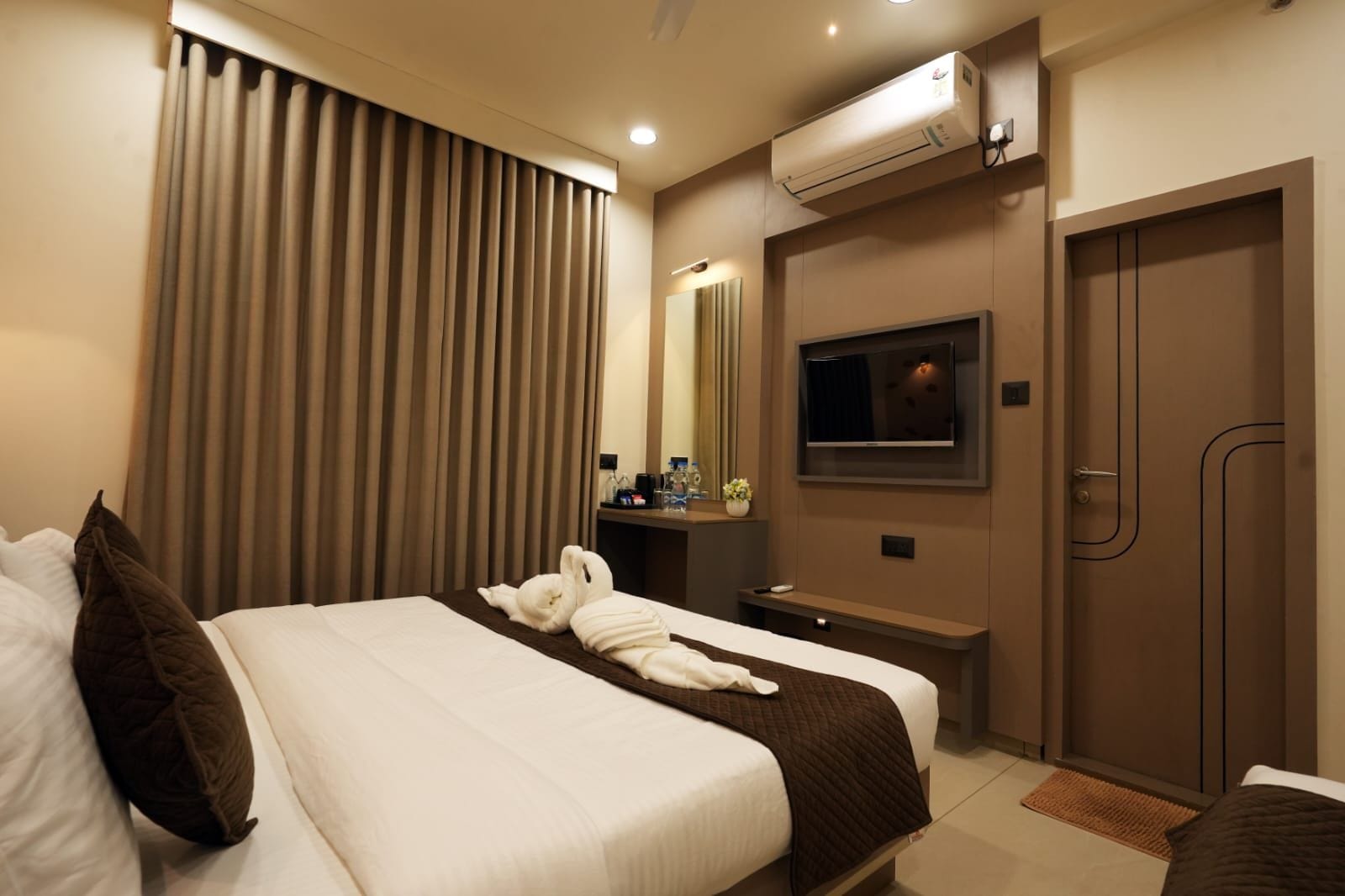 A hotel room with a bed, a TV, a mirror, and a wardrobe.