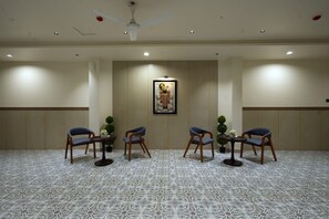 A conference room with a patterned carpet, wooden chairs, a ceiling fan, recessed lighting, and a framed picture on the wall. - Hotel The Dwarka palace (Dwarka)