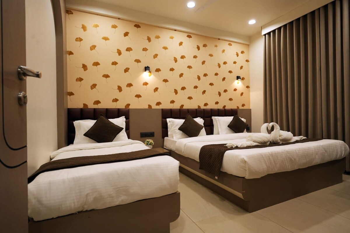 A hotel room with two beds, a wall with leaf patterns, and a curtain.