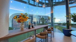 A modern interior with a curved glass wall, a bar area with seating, and a decorative bird sculpture. - Modern New 1 BR Condo(BWC2) (Hua Hin)