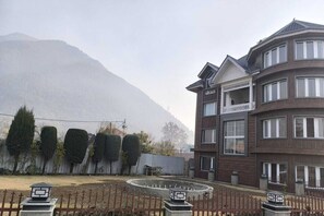 Un edificio de varios pisos con un balcón, rodeado por una zona vallada que incluye un elemento acuático circular.