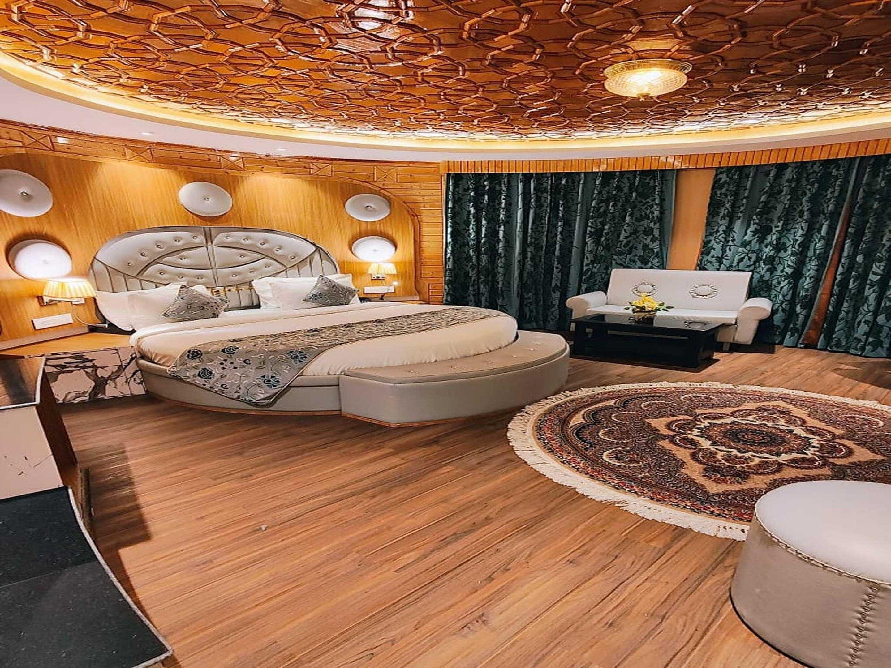 A luxurious bedroom with a large bed, a round seating area, and a unique ceiling design.