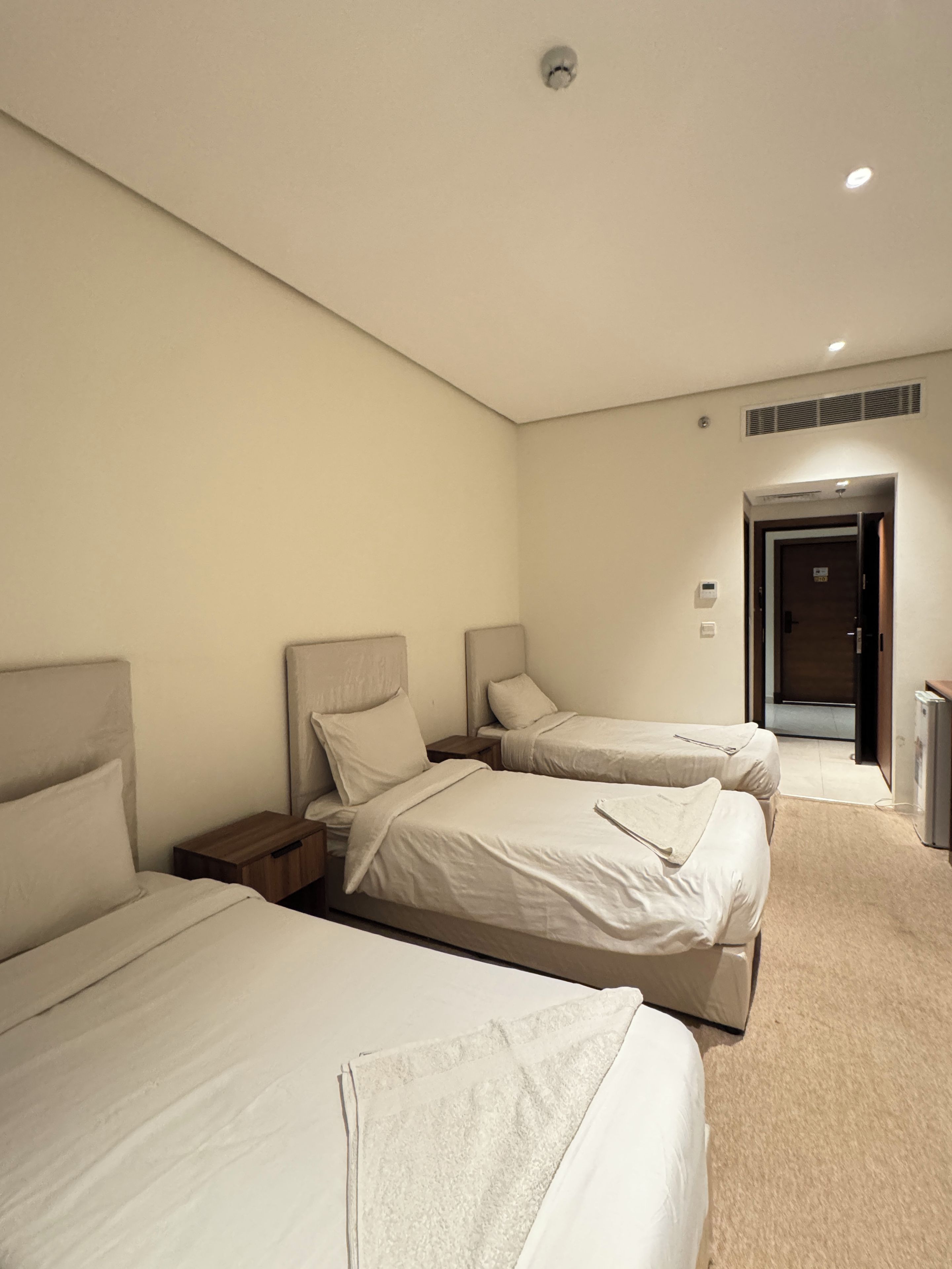 Ein Hotelzimmer mit drei Betten, einer Tür und einem kleinen Schreibtisch.