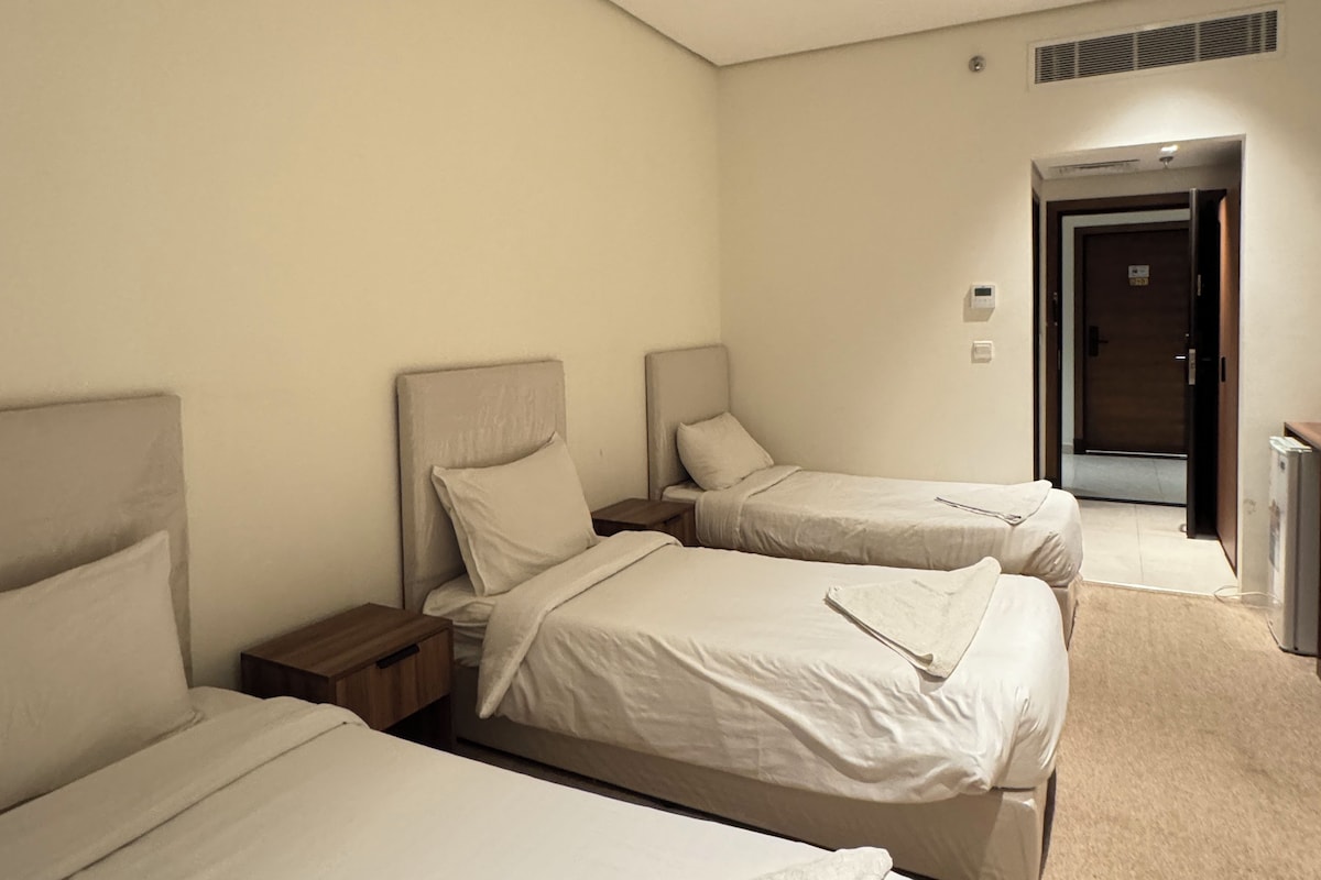 A hotel room with three beds, a door, and a small desk.