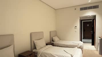 Ein Hotelzimmer mit drei Betten, einer Tür und einem kleinen Schreibtisch.