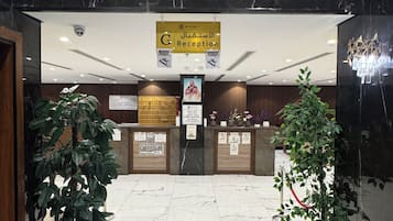 Un área de recepción con piso de mármol, plantas en macetas y un cartel que indica la recepción.