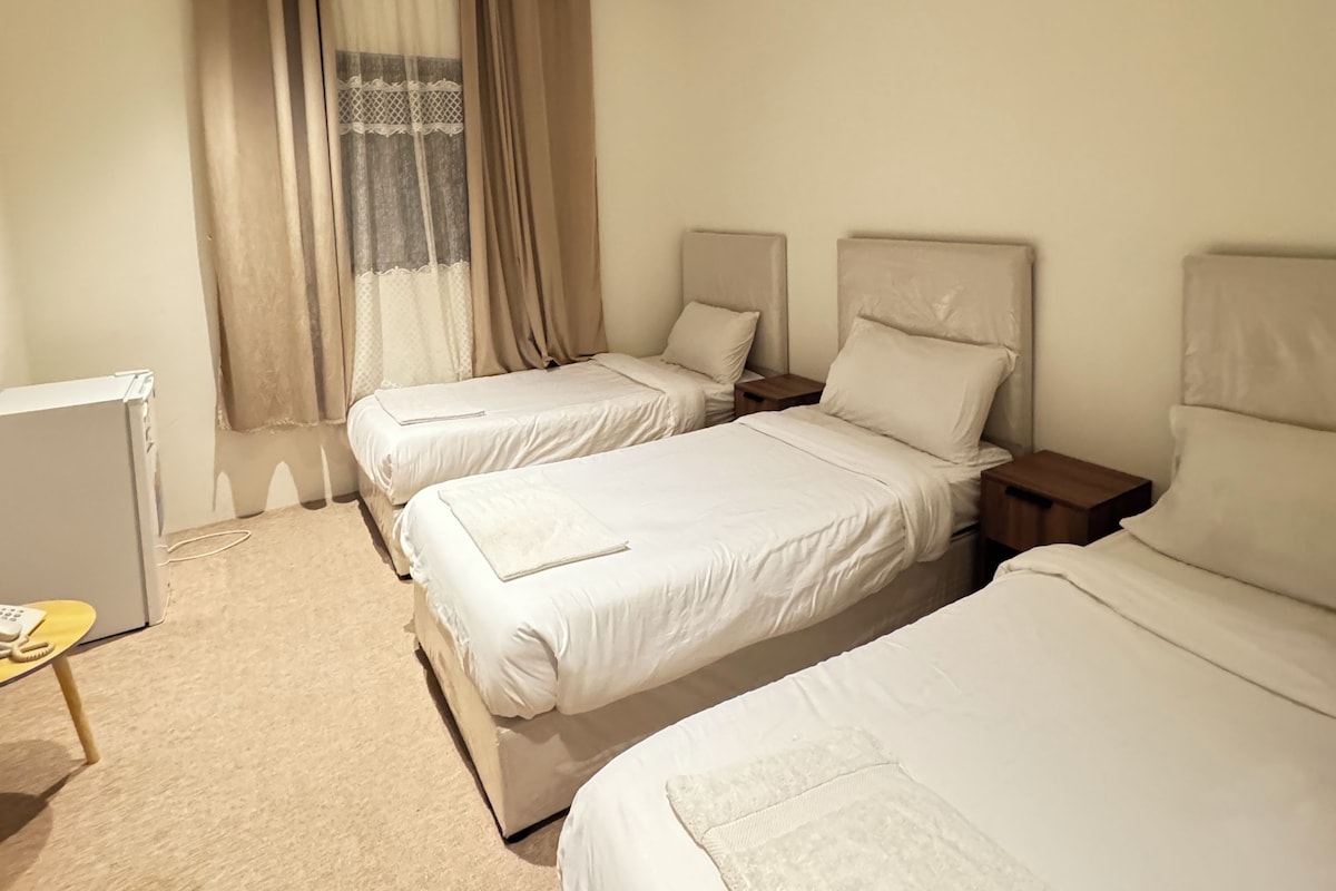 A hotel room with two beds, a small table, and a window with curtains.