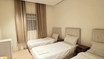A hotel room with two beds, a small table, and a window with curtains.